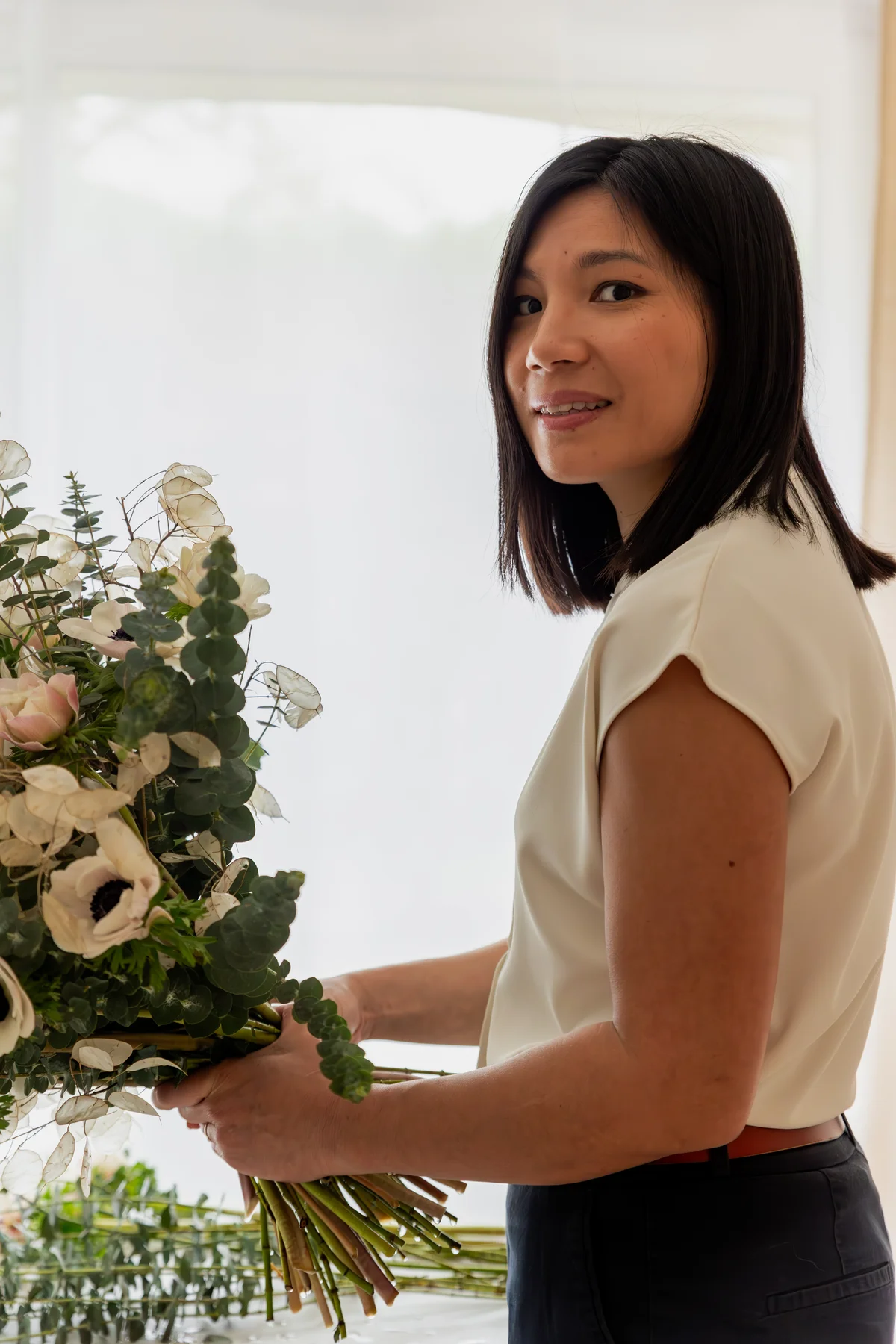 Lucille Cha, designer florale certifiée et créatrice de A Sparkling Moment, en train de composer un grand bouquet champêtre avec eucalyptus, anémones blanches et monnaie du pape dans son atelier près d'Amboise en Touraine.